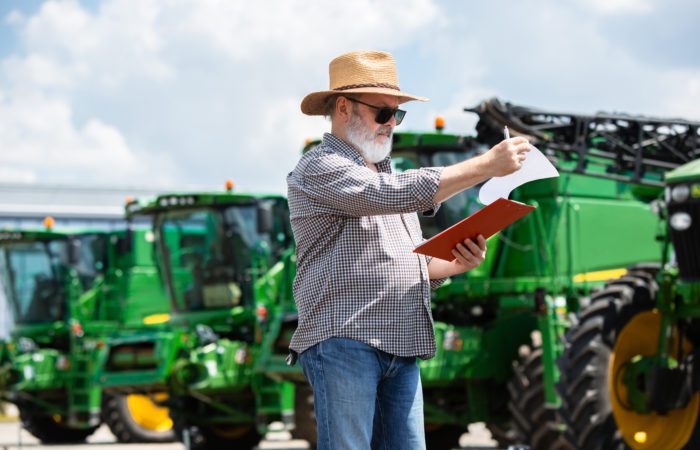 Professional farmer with a modern combine at field in sunlight at work. Confident, bright summer colors. Agriculture, exhibition, machinery, plant production. Senior man near his tractor with investor.